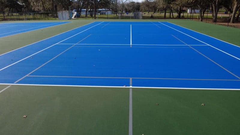 Close-up aerial view of freshly resurfaced tennis court with crisp white lines and green playing surface