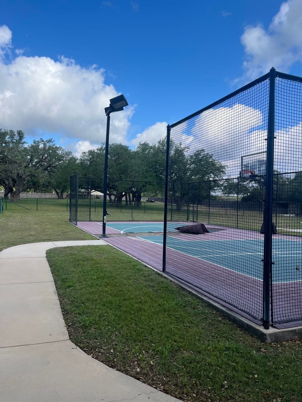 Before photo of a worn, faded multi-sport tile court with cracked teal and maroon surface in Wimberley, Texas