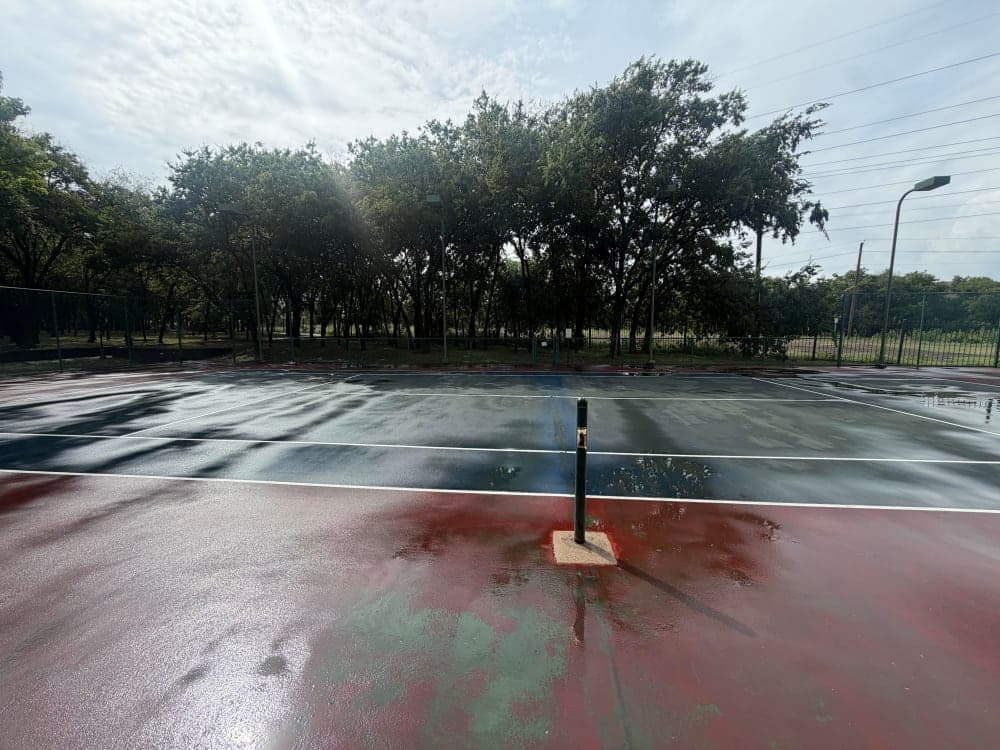 Weathered red and blue tennis court with a faded, worn surface before conversion in Richardson, Texas