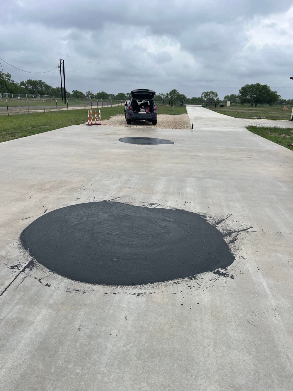 Repaired low spots sealed with black coating on the pickleball court slab near San Antonio, Texas