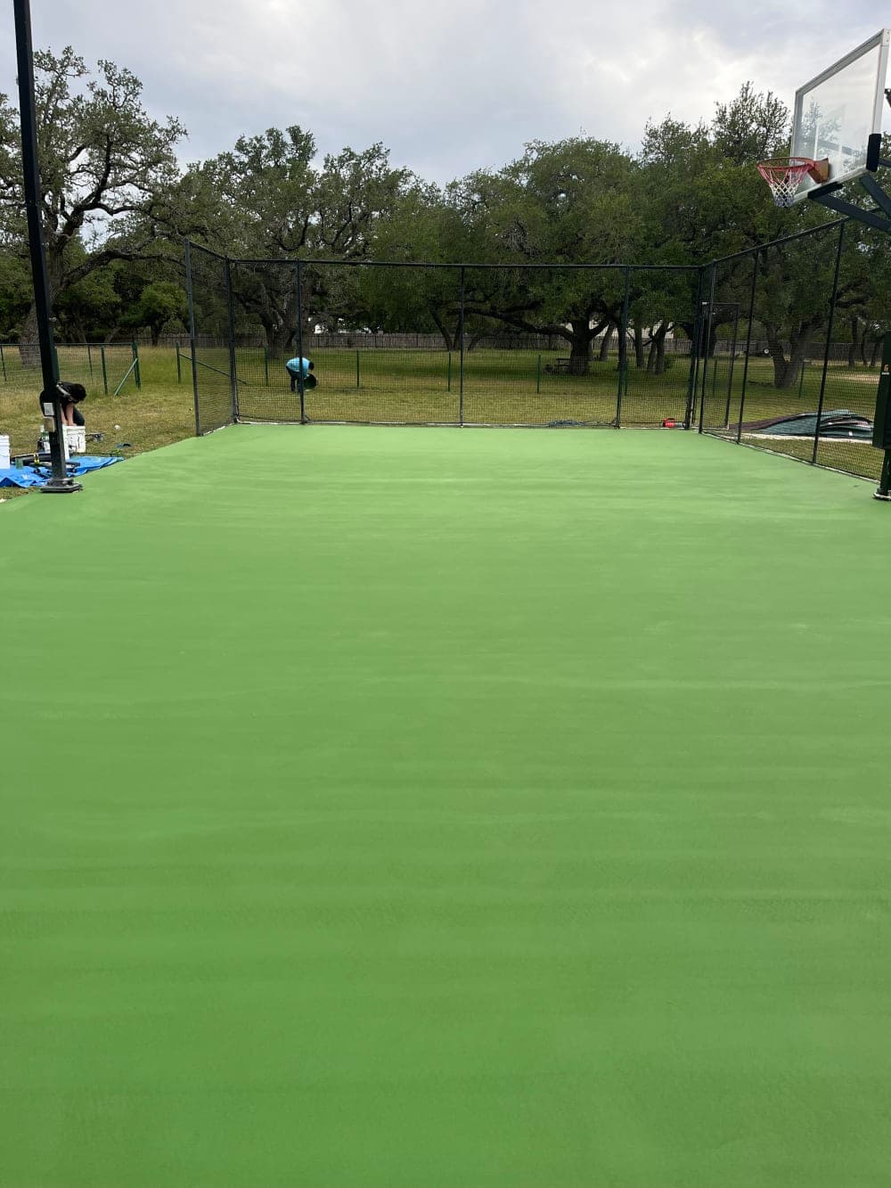Green acrylic color coat going down on the resurfaced court in Wimberley, Texas