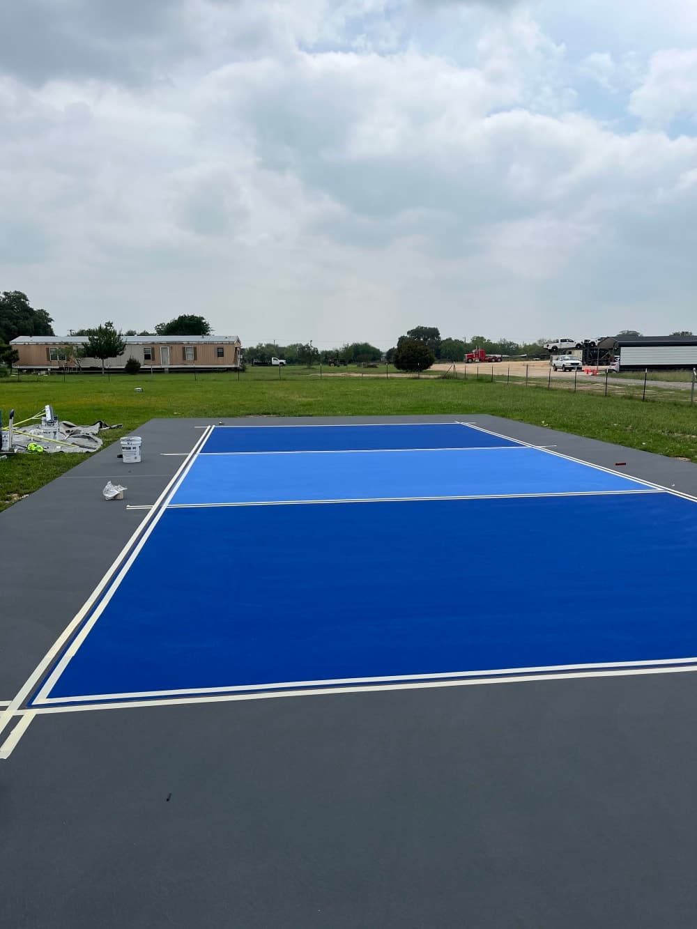 Pickleball court lines masked out in tape over the blue and gray surface before striping near San Antonio, Texas