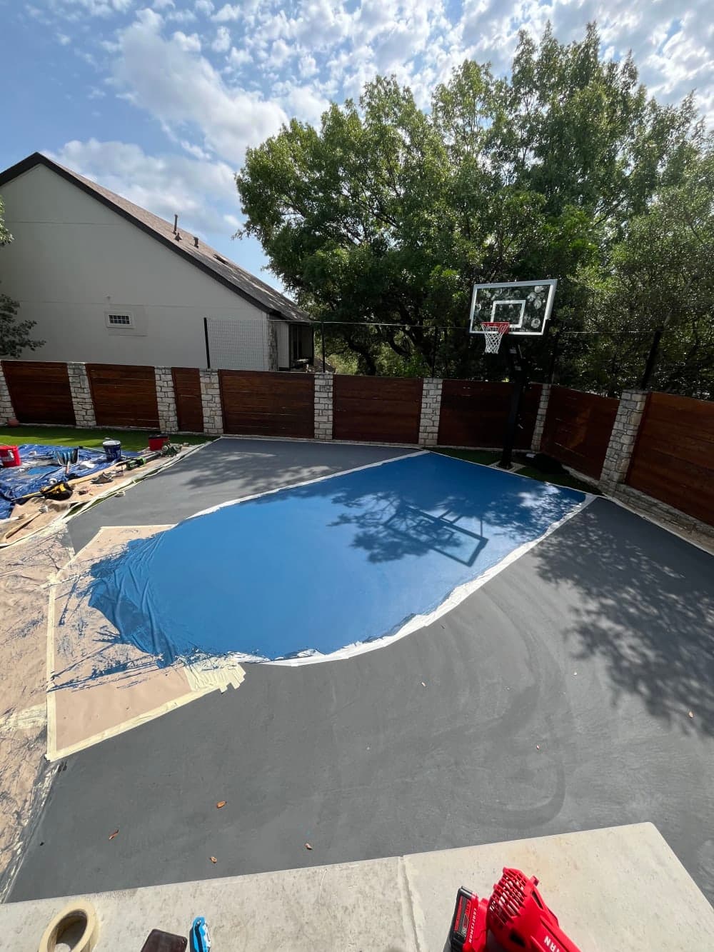Blue key color coat going down over the gray backyard basketball court before striping in Austin, Texas
