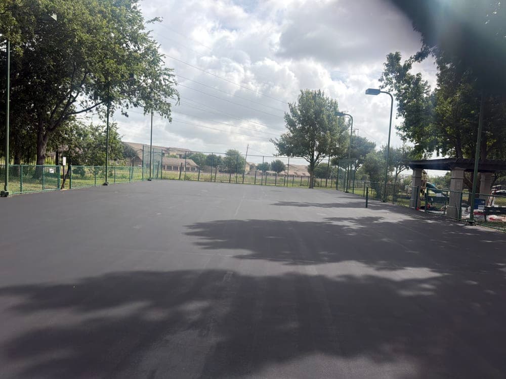 The old tennis court resurfaced with a fresh gray base coat, prepped for new color zones, in Richardson, Texas