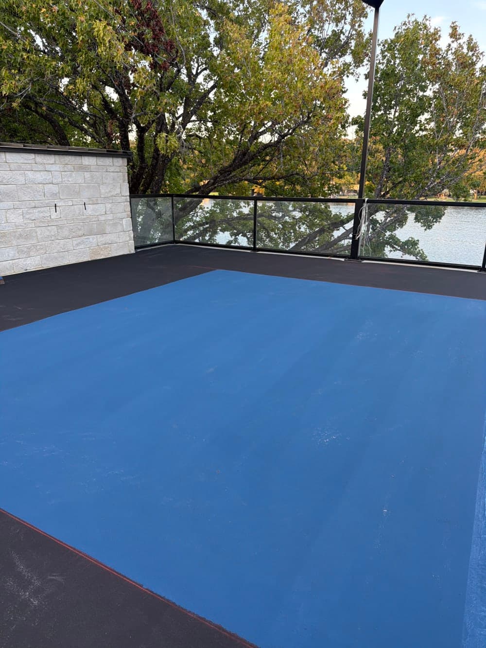 Black acrylic base coat with the first blue color coat going down on the rooftop court deck on Lake Austin, Texas