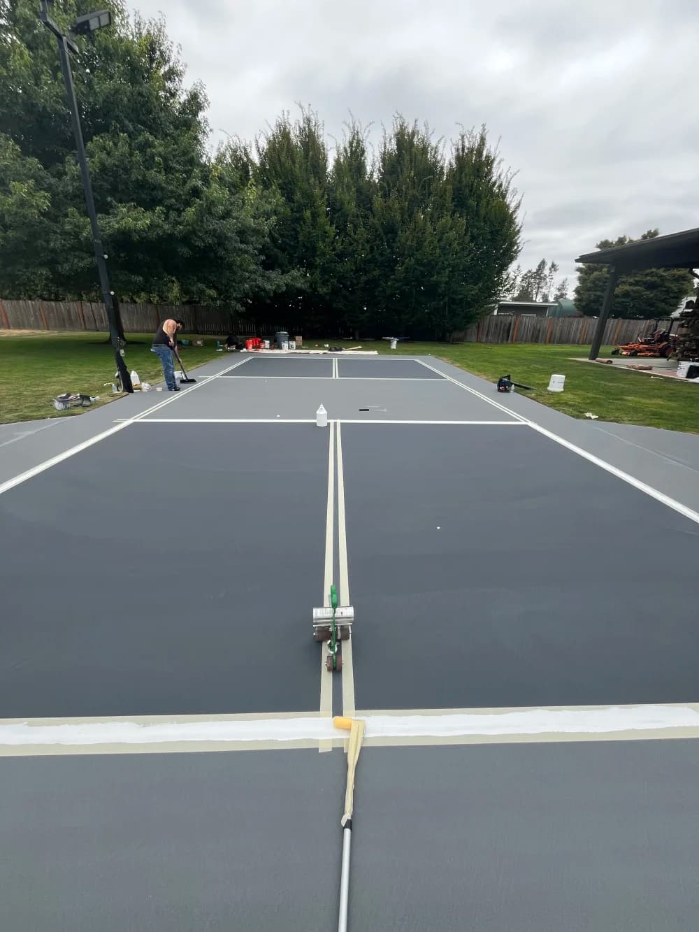 Crew taping and painting crisp white pickleball lines on the slate and gray court in Sumner, Washington