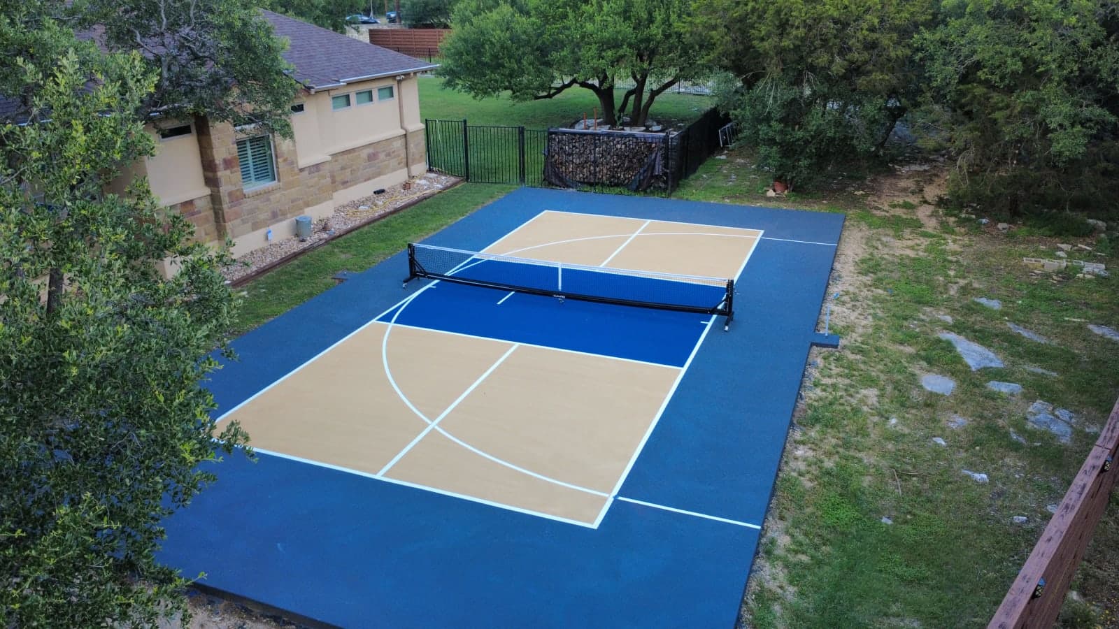 Aerial view of a finished blue and gold backyard basketball and pickleball court in Georgetown, Texas
