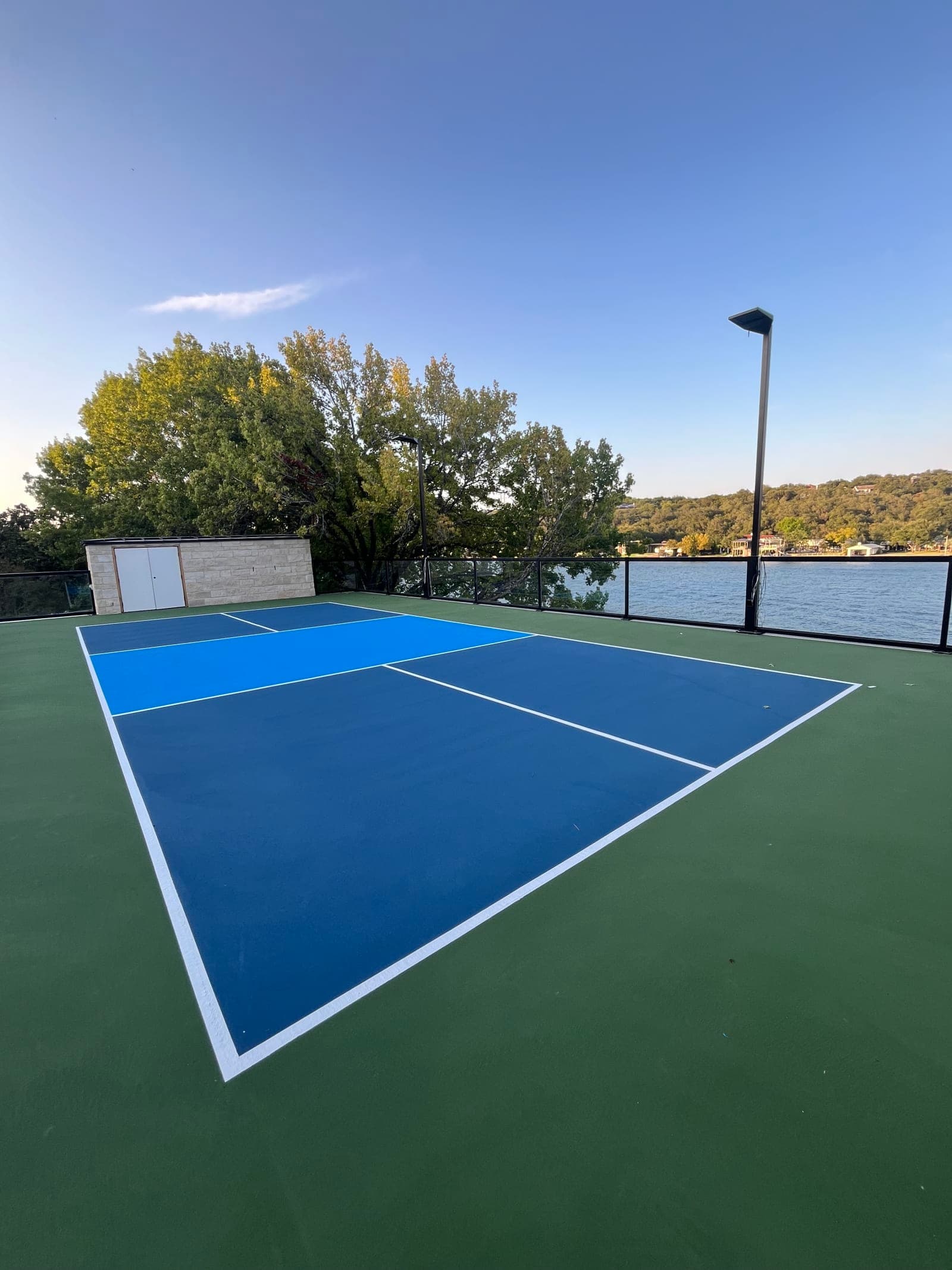 Finished navy and light blue rooftop pickleball court with a green surround and glass railing overlooking Lake Austin in Austin, Texas