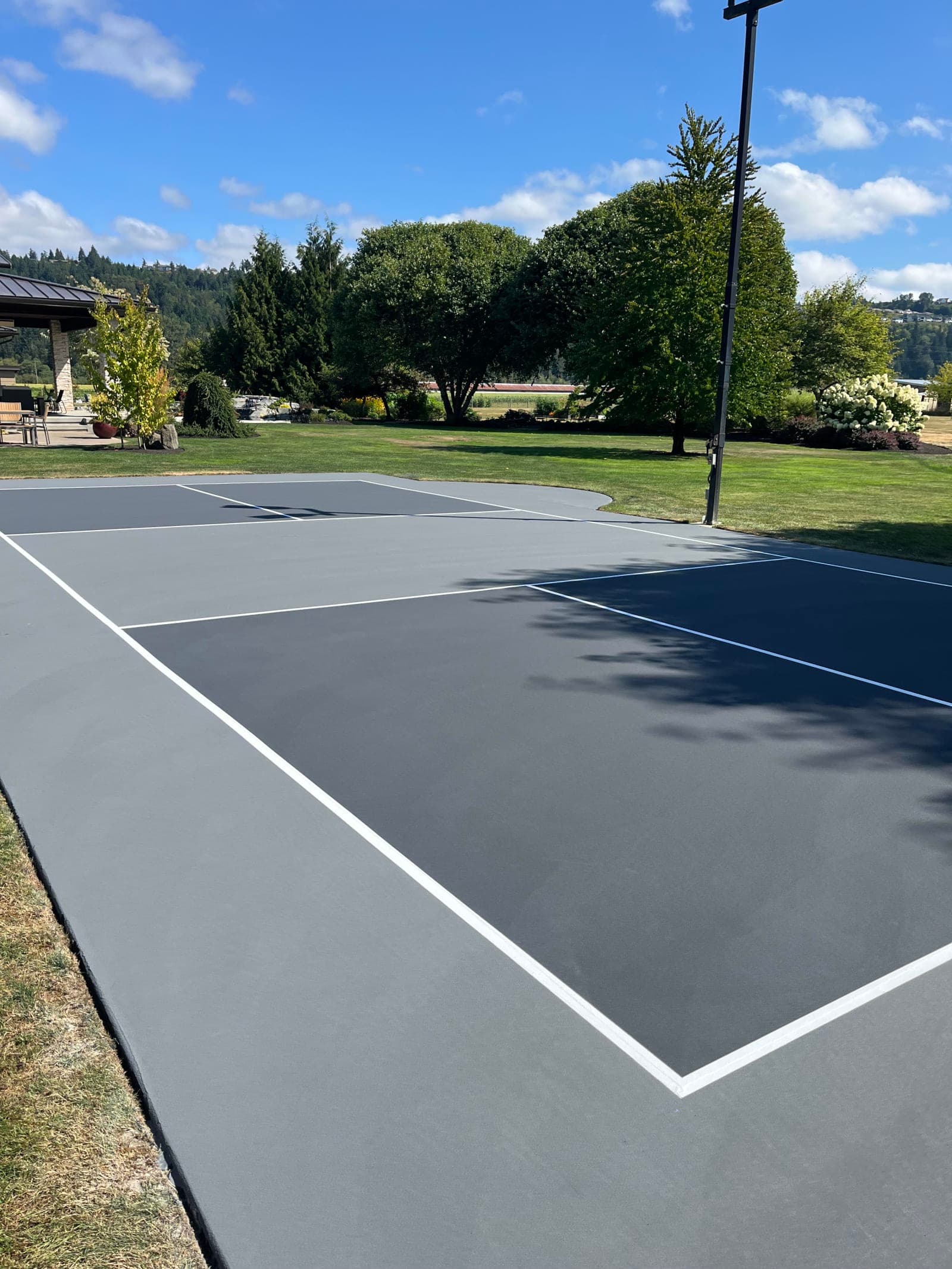 Finished slate and gray backyard pickleball court with white lines and a covered pavilion in Sumner, Washington